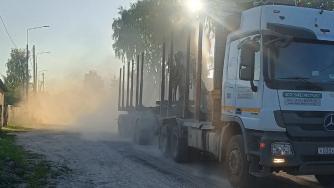 Лесовоз едет по грунтовке на улице в Пудоже, пыль столбом