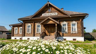 деревянный дом культуры, перед ним клумба с ромашками