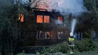 пожарные тушат горящий многоквартирный деревянный дом
