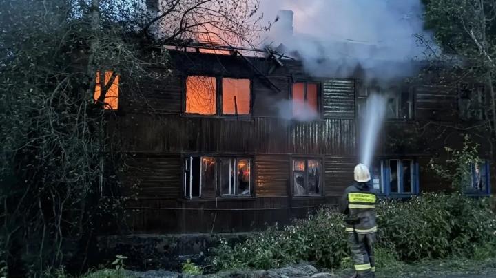 пожарные тушат горящий многоквартирный деревянный дом