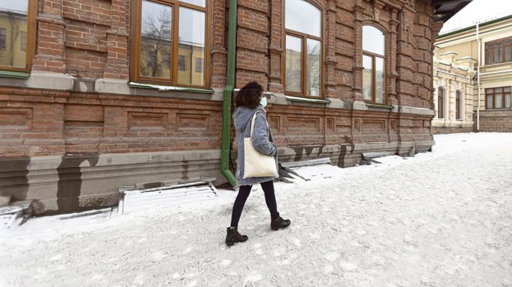 Женщина идет по заснеженному тротуару в городе.